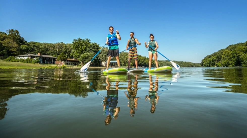 Paddle boarders on a Bella Vista lake, with lakeside homes on the far shore